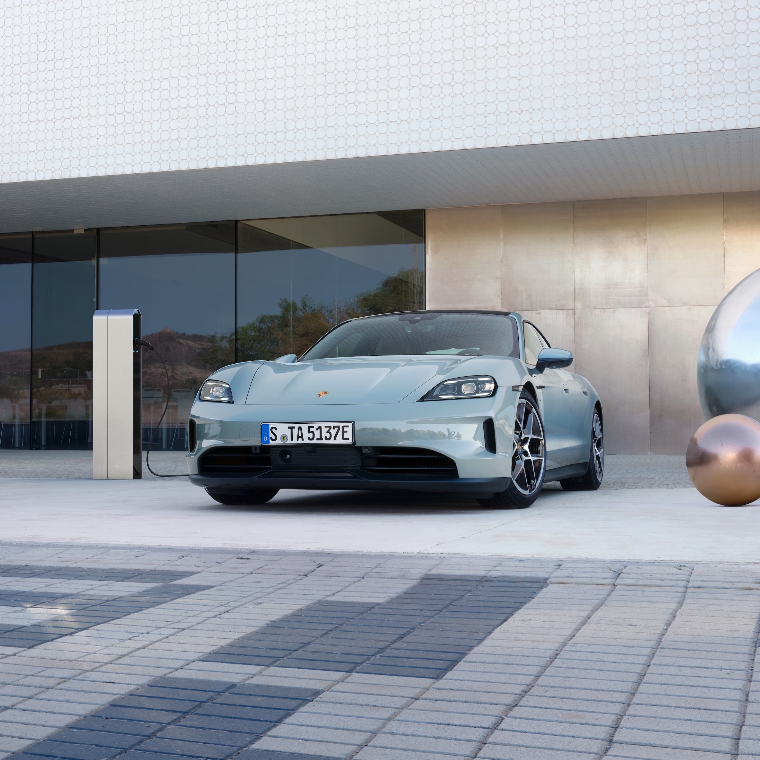 Une Porsche Taycan garée devant un immeuble moderne.